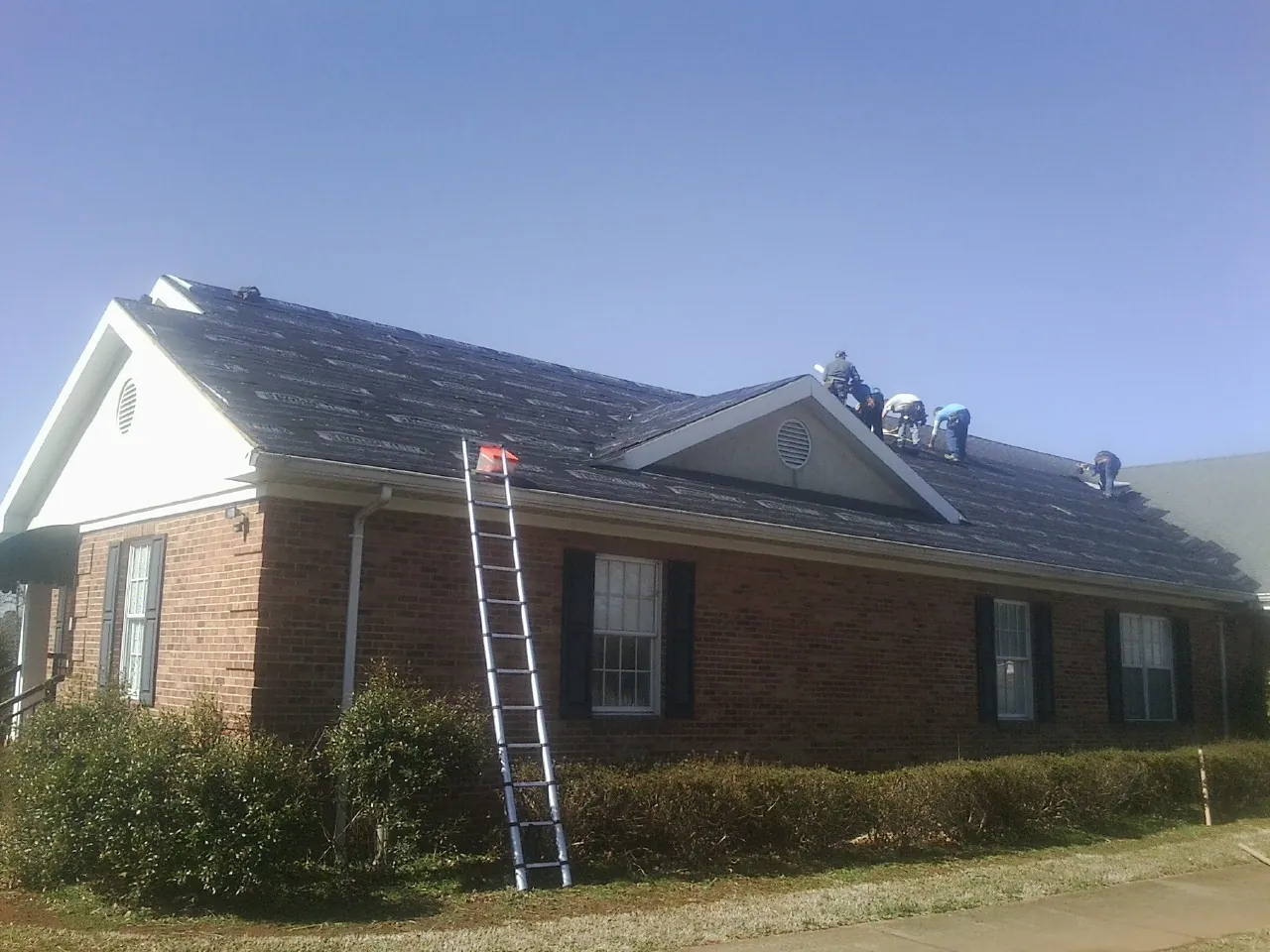 Crew tearing shingles off a brick ranch roof with a ladder set — Metal Roof Repair work by our crew in Leola