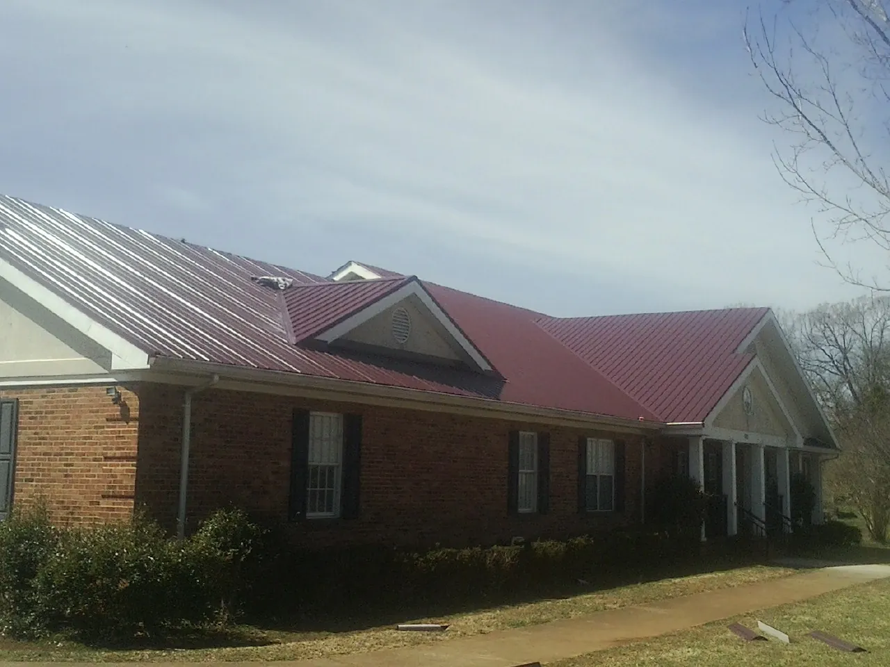 Red metal roof with gabled entries on a long brick building, from a Hail Damage Roof Repair job in Leola