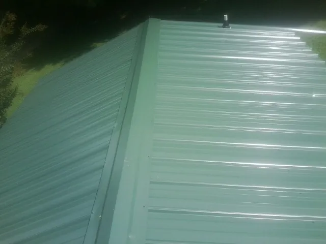 New green metal panels meeting at the ridge of a roof — Flat Roof Repair work by our crew in Leola