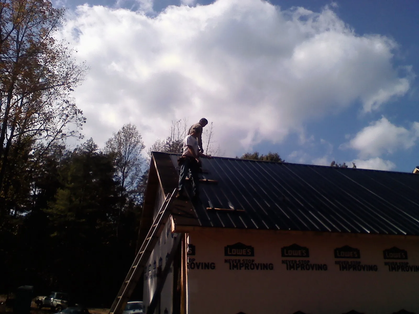 Roofer fastening dark metal panels high against a cloudy sky, from a Roof Inspection job in Leola