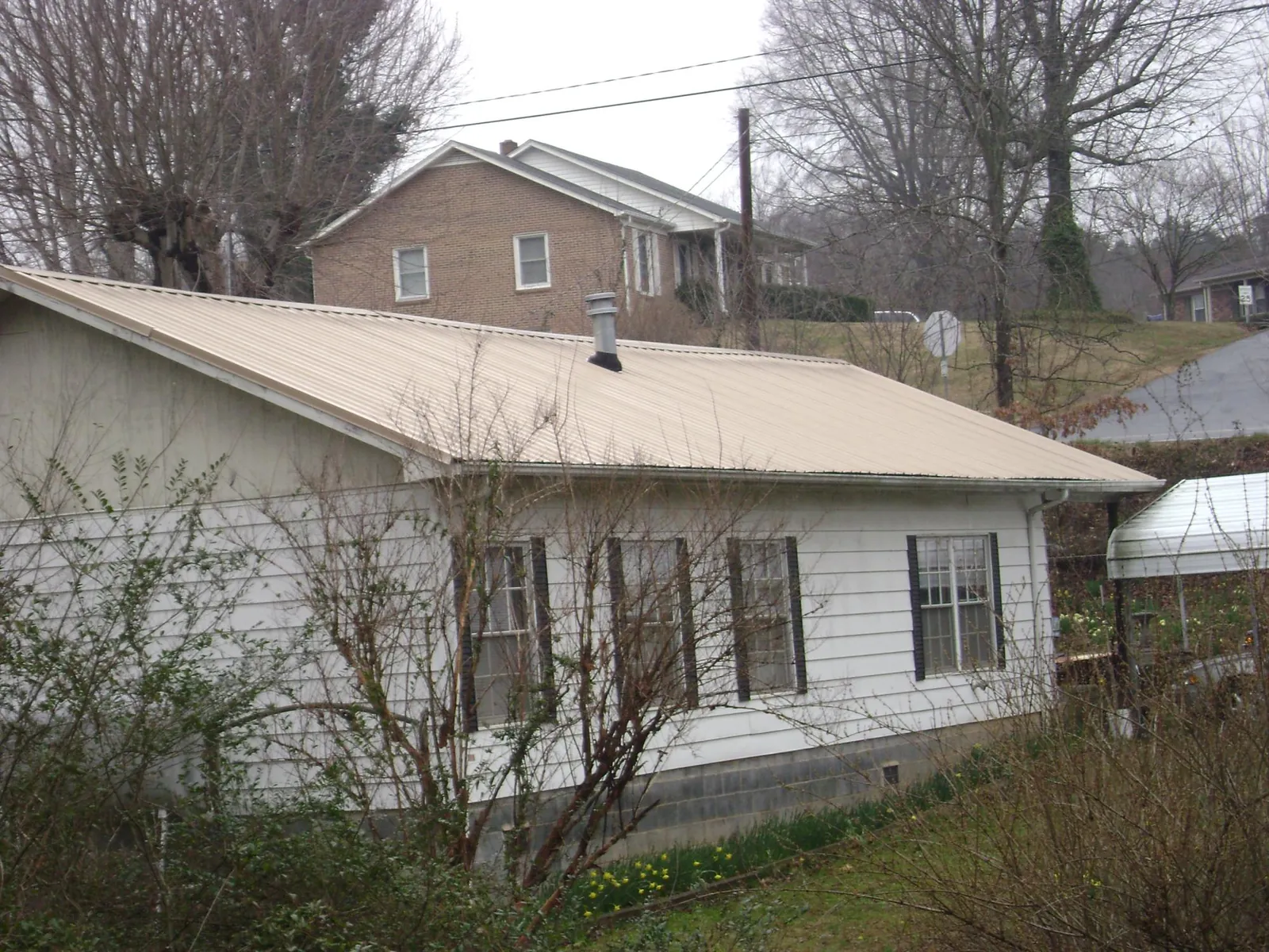 Tan metal roof on a white sided house set into a hillside — Commercial Roofing by Roofing Brothers in Leola